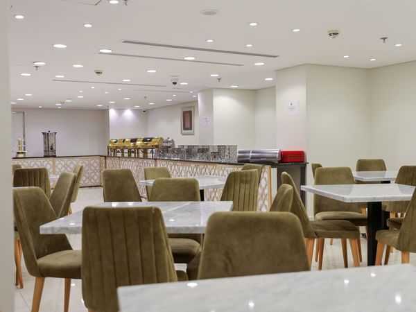 A dining area with white marble tables and green upholstered chairs at Saja by Warwick Makkah.