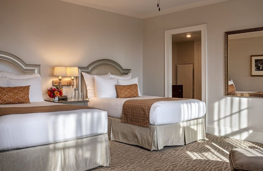 Two beds with arched headboards by wall lamps under a ceiling fan in Deluxe Double at Warwick Melrose Dallas