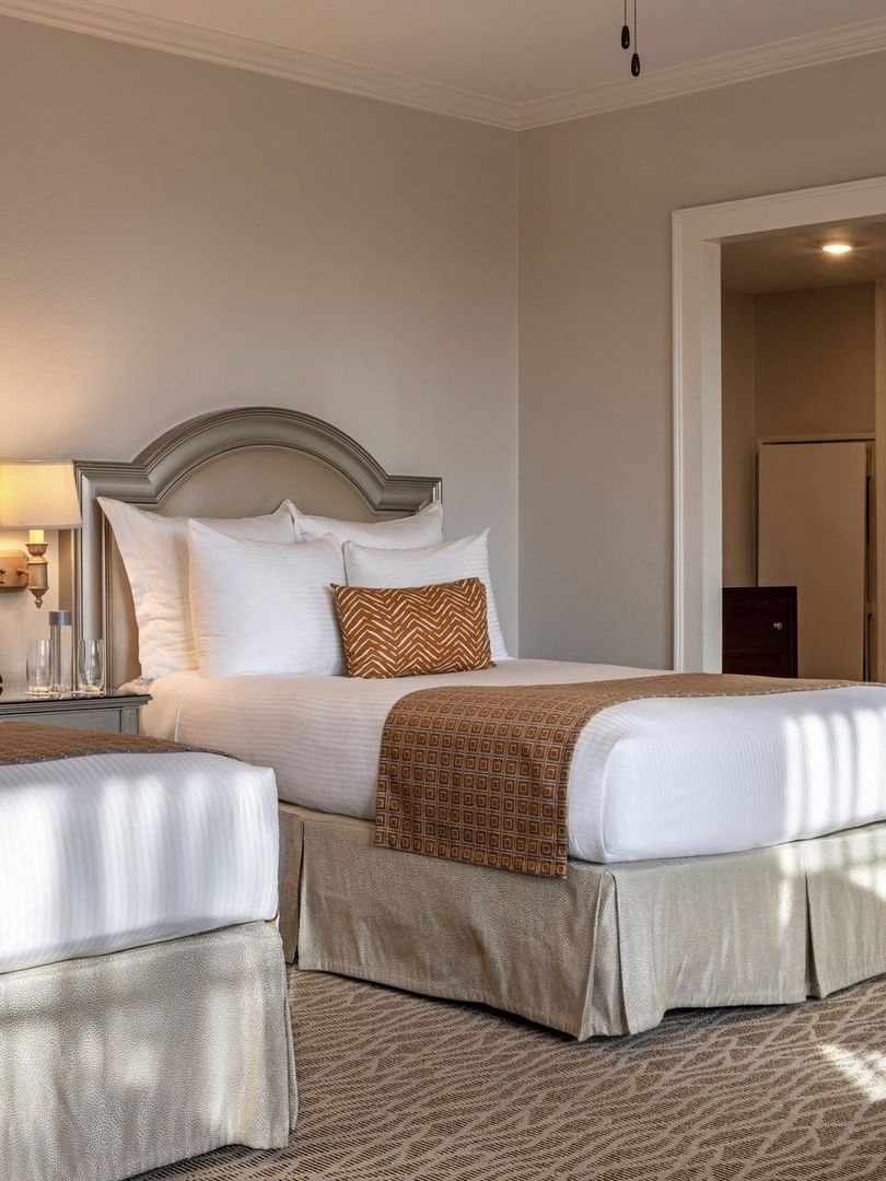 Two beds with arched headboards by wall lamps under a ceiling fan in Deluxe Double at Warwick Melrose Dallas