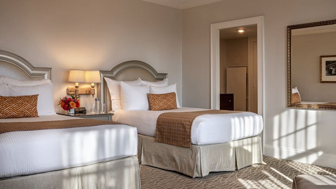 Two beds with arched headboards by wall lamps under a ceiling fan in Deluxe Double at Warwick Melrose Dallas