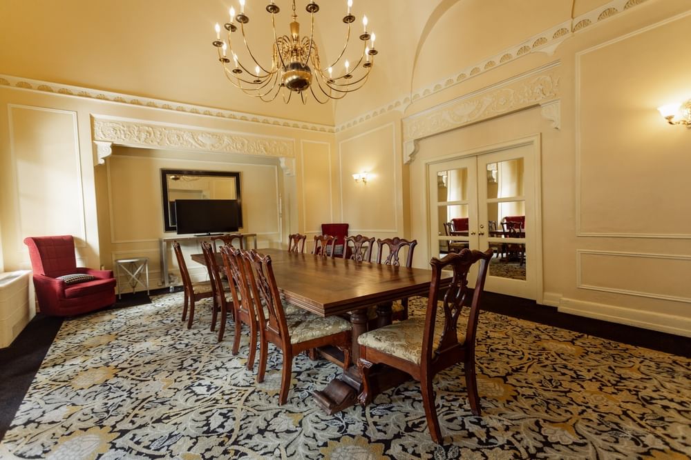 Long wooden table with chairs on a patterned rug under a gold chandelier in the Board Room at Arlington Resort Hotel & Spa