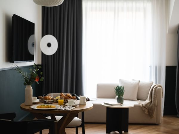 Cozy TV lounge and dining area featuring a table set with croissants, eggs, and juice at Almanac X Alcron Prague