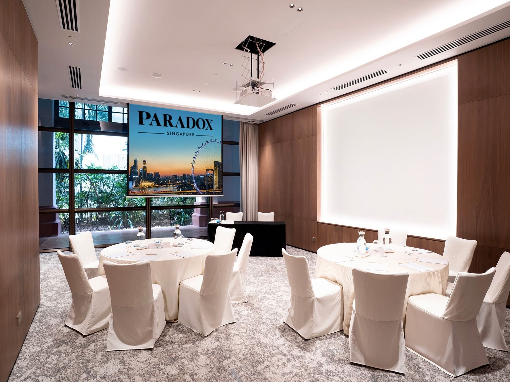 Cluster setup in a meeting room at Paradox Singapore, featuring small groups of tables and chairs arranged for breakout discussions in a contemporary, professional setting.