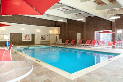 Indoor swimming pool with bright blue water, red umbrellas, and lounge chairs at White River Inn and Suites