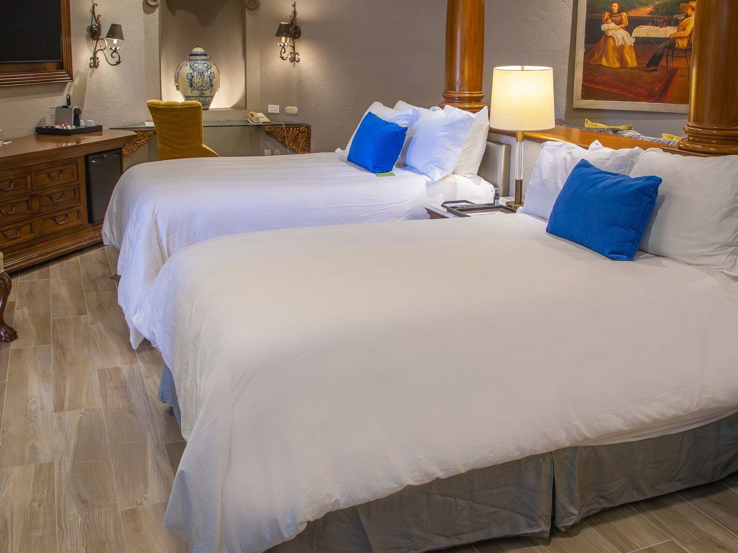 Suite elegante con dos camas dobles, ropa blanca, cojines azules y decoración colonial en Quinta Real Guadalajara