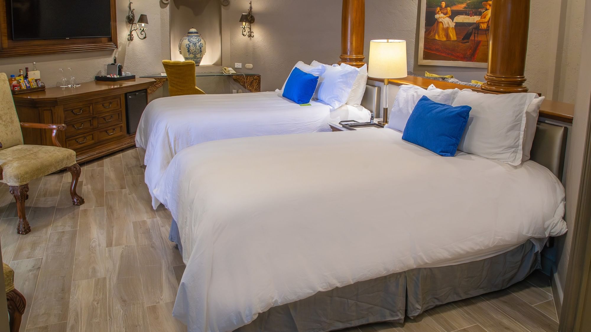 Suite elegante con dos camas dobles, ropa blanca, cojines azules y decoración colonial en Quinta Real Guadalajara