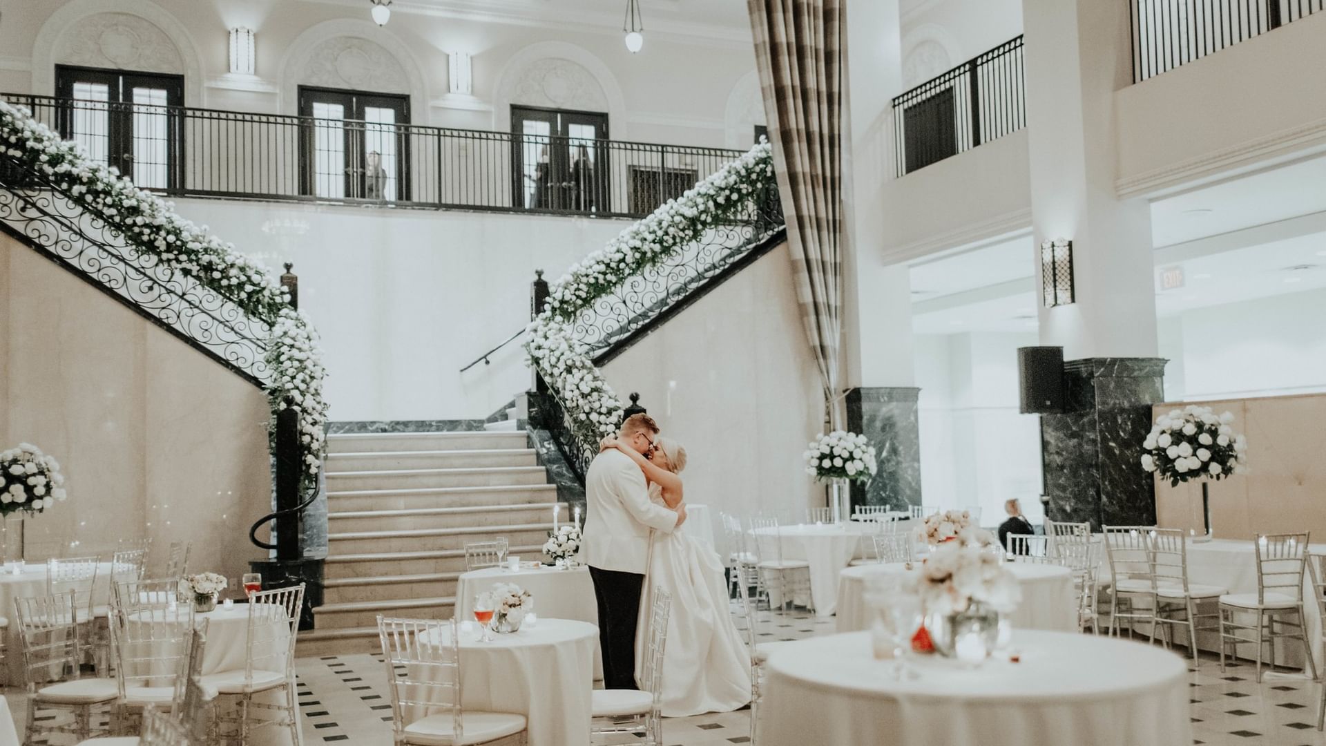 Grand Hall at The Mayo Hotel in Tulsa with a couple embracing among decorated tables and a grand staircase.