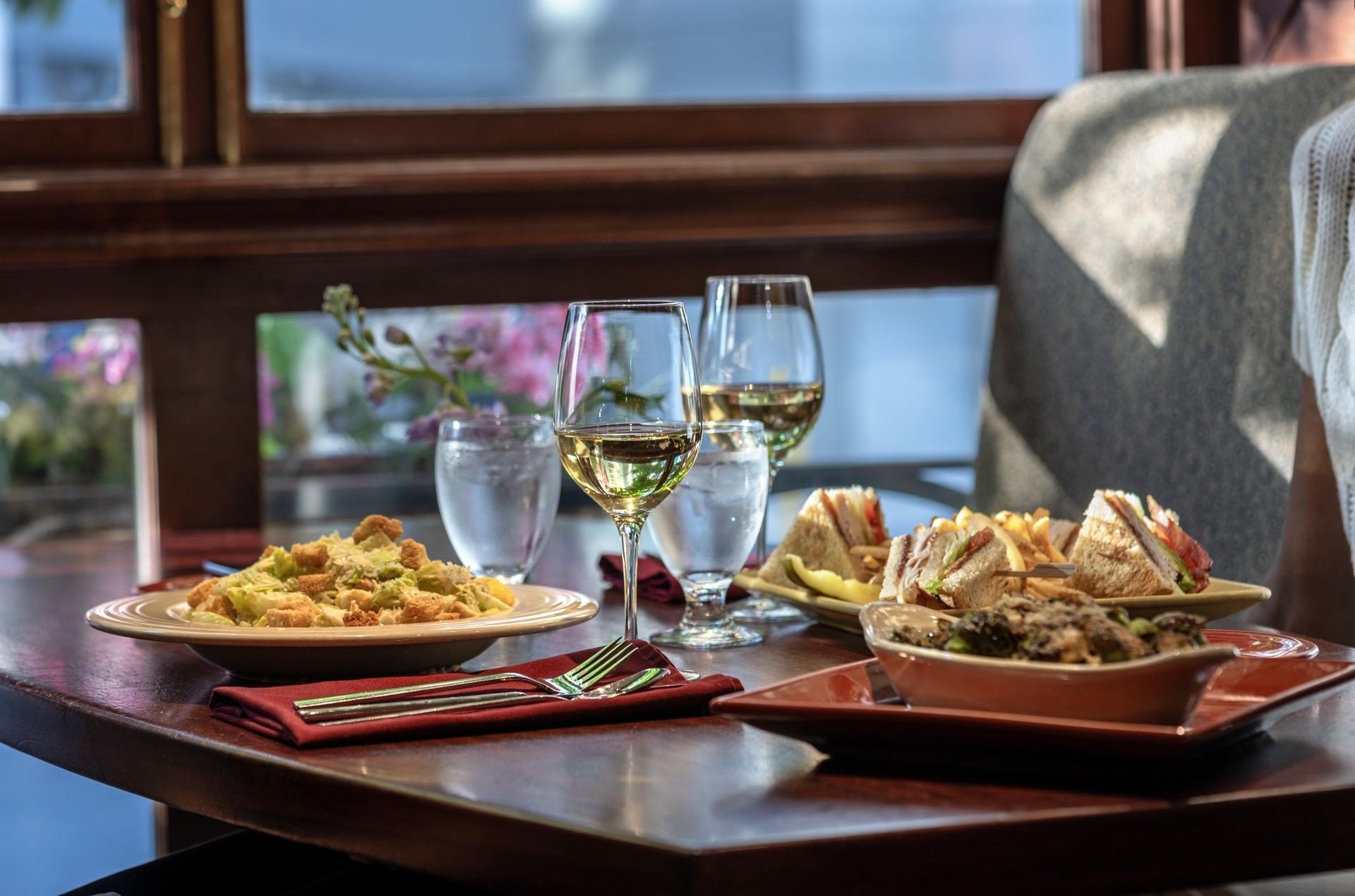 salad and club sandwiches by wine glasses on table in Margaux Restaurant at Warwick Seattle