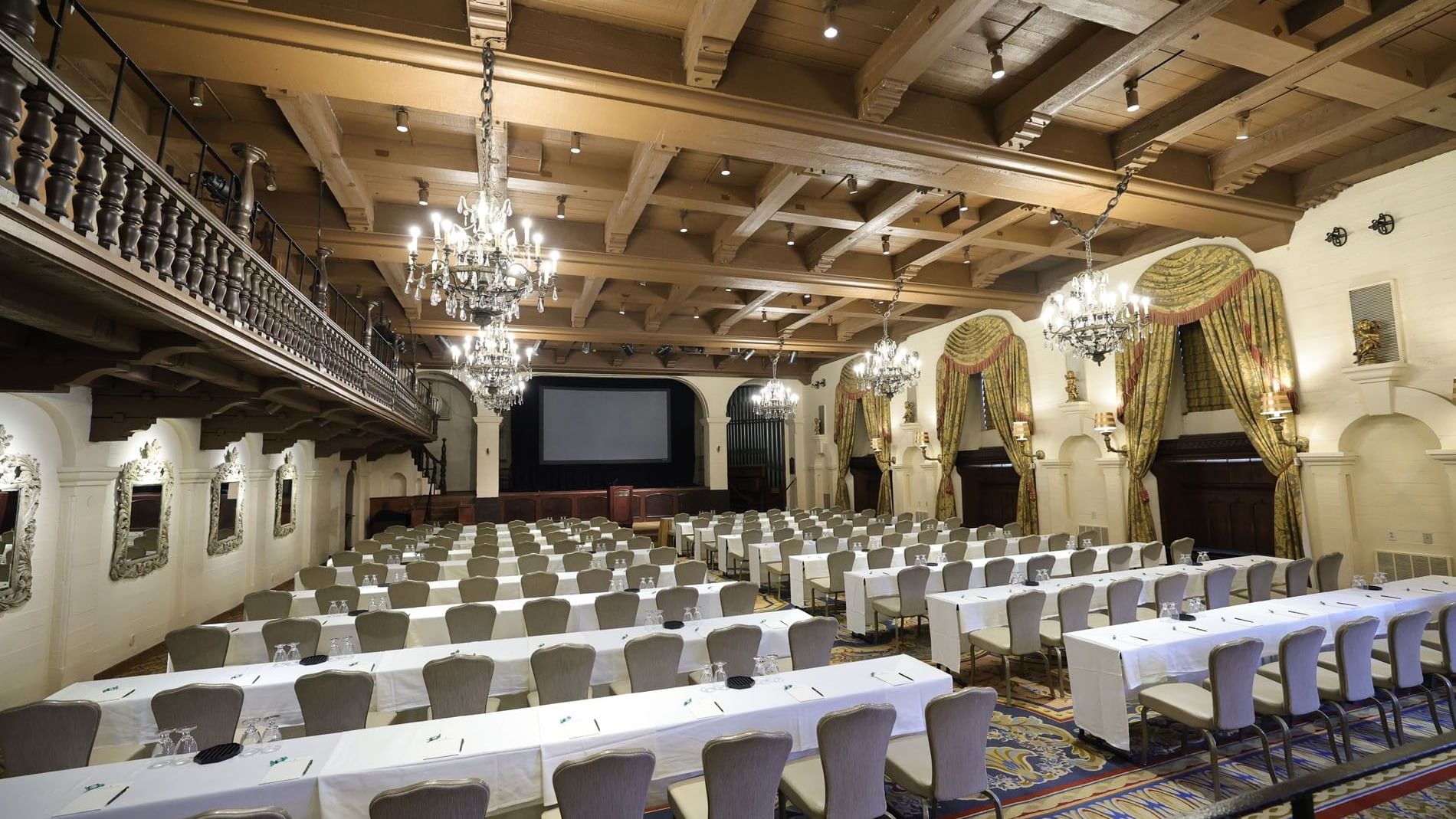 Classroom setup facing the stage with a projector screen under chandeliers in The Grand Parisian Ballroom at The Mission Inn