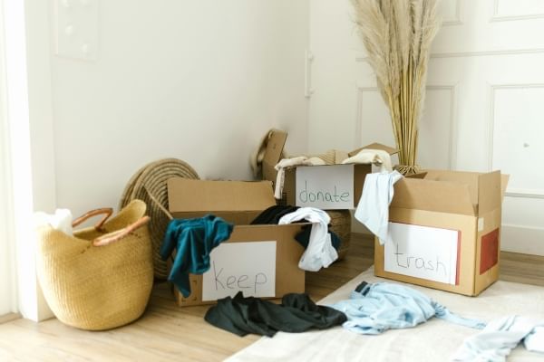 Three boxes with clothes strewn around labeled “donate,” “keep,” and “trash” in a white room. 