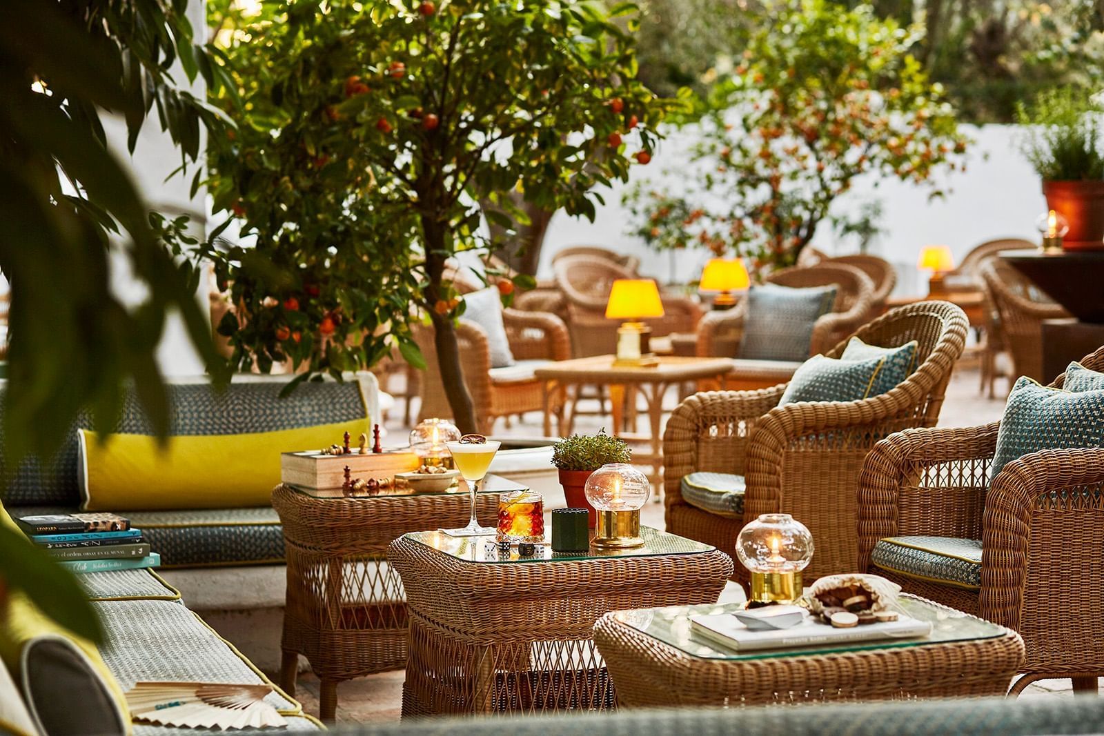 Cozy Marbella Club outdoor lounge beneath orange trees with wicker chairs and cocktails on tables