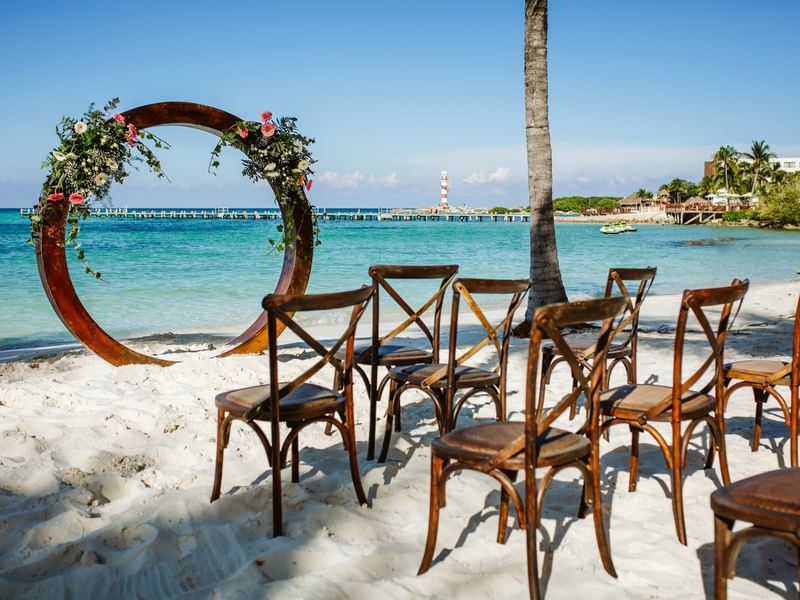 Beach wedding ceremony with wooden chairs and a flower arch at Grand Fiesta Americana Hotel and Resorts