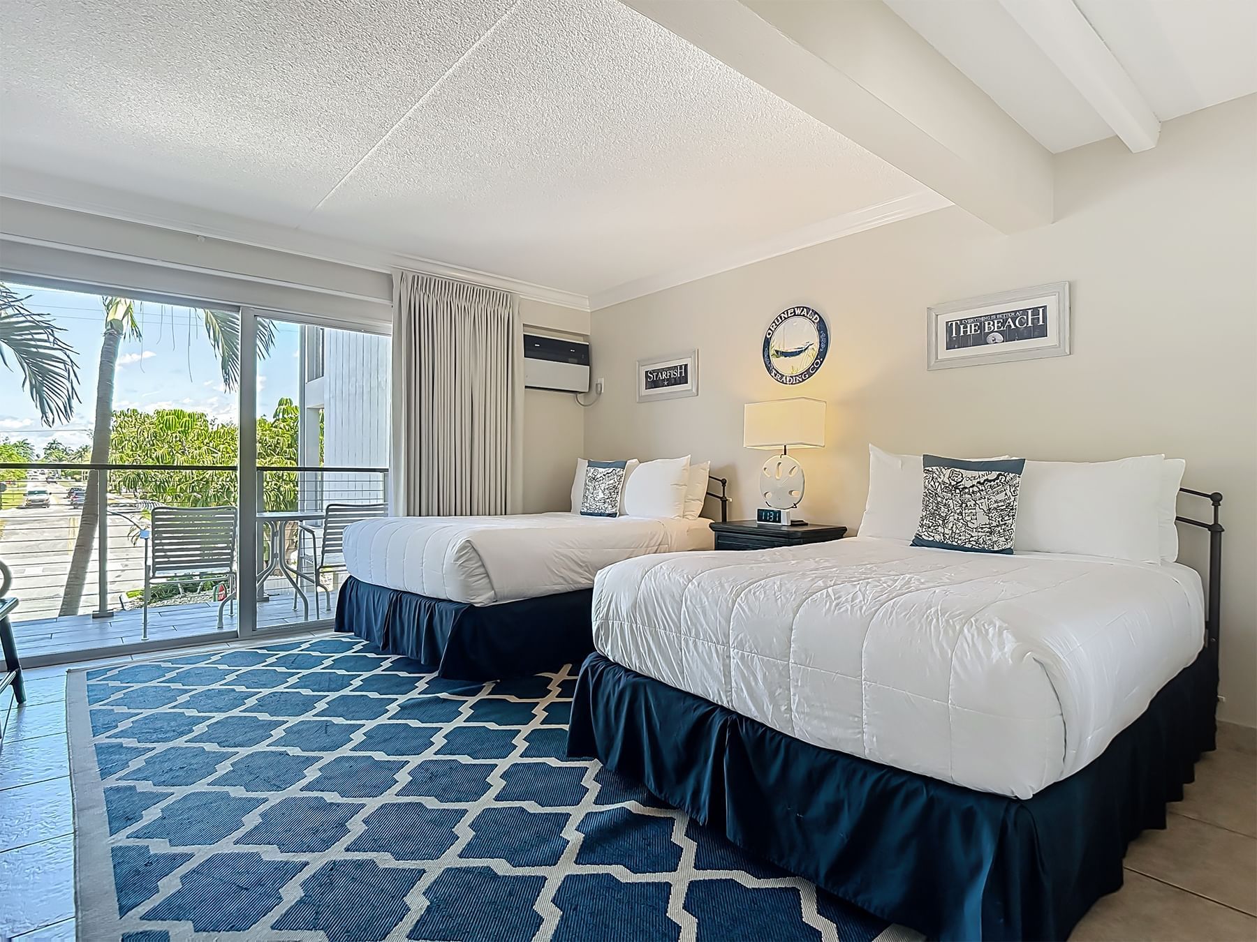 Two cozy beds with white linens and a balcony view at Cove Inn at Naples Bay in Naples.