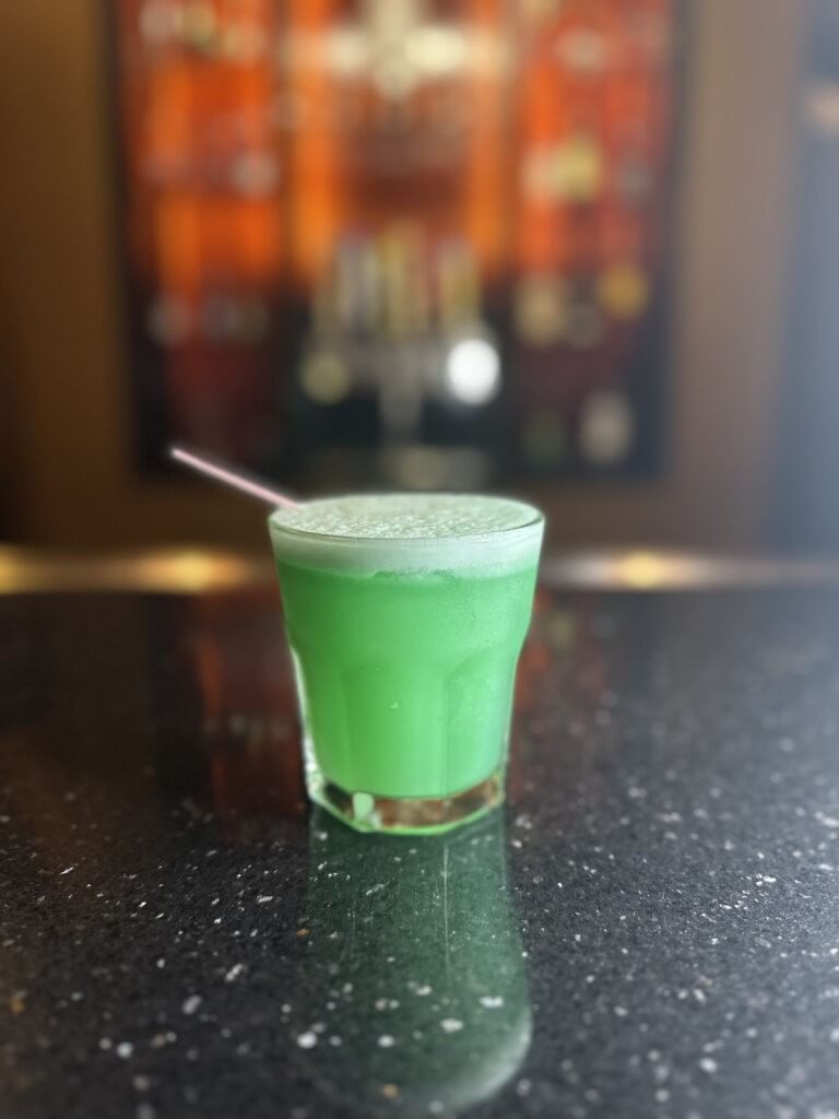 A bright green cocktail sitting on a black granite bar.