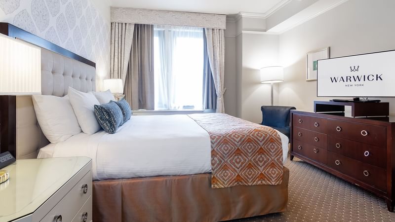 Cozy bed with side tables and working table in On The Avenue One Bedroom Suite at Warwick New York