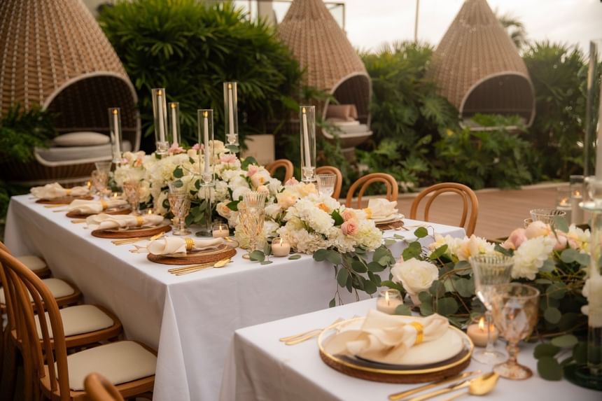 Elegant outdoor dining table with white floral centerpieces, gold flatware, and woven cabanas at Almar LGBT Luxury Resort