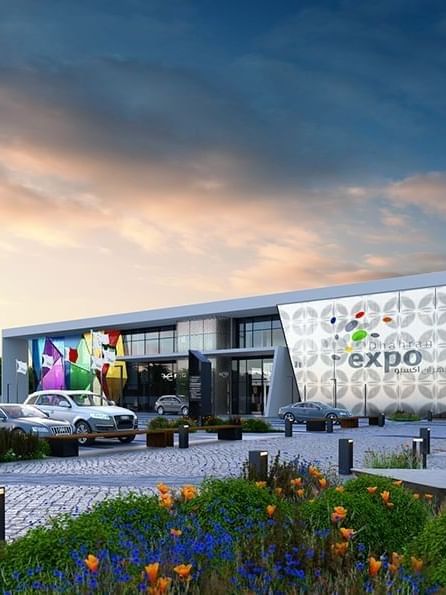 Dhahran Expo by parked cars under a soft sunset sky with vibrant banners near Warwick Al Khobar