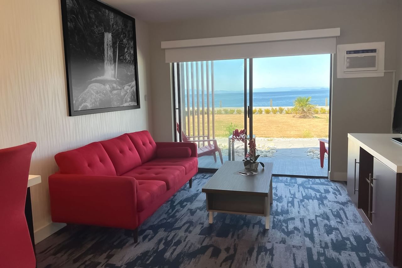 Living area of guest room with tv, coffee table, red couch, patio doors, view of sea