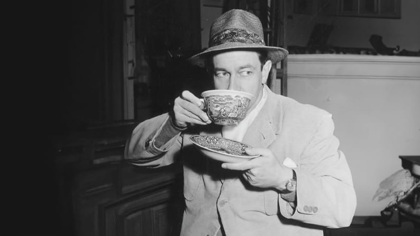 Grayscale picture of a man in a vintage suit and hat sipping tea at Paramount Hotel Dubai