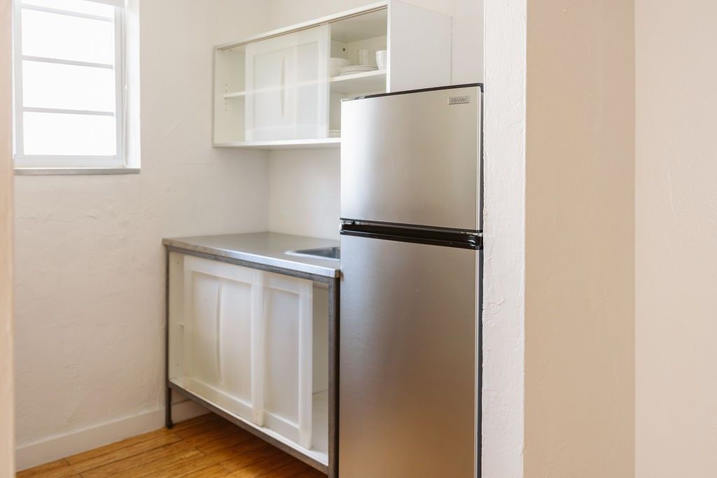 A small kitchenette with a stainless steel refrigerator, sink, and white cabinets.