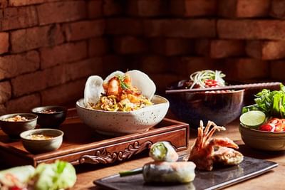 Beautifully arranged table with bowl of shrimp noodle dish & fresh spring rolls in Square One Restaurant at Park Hyatt Saigon
