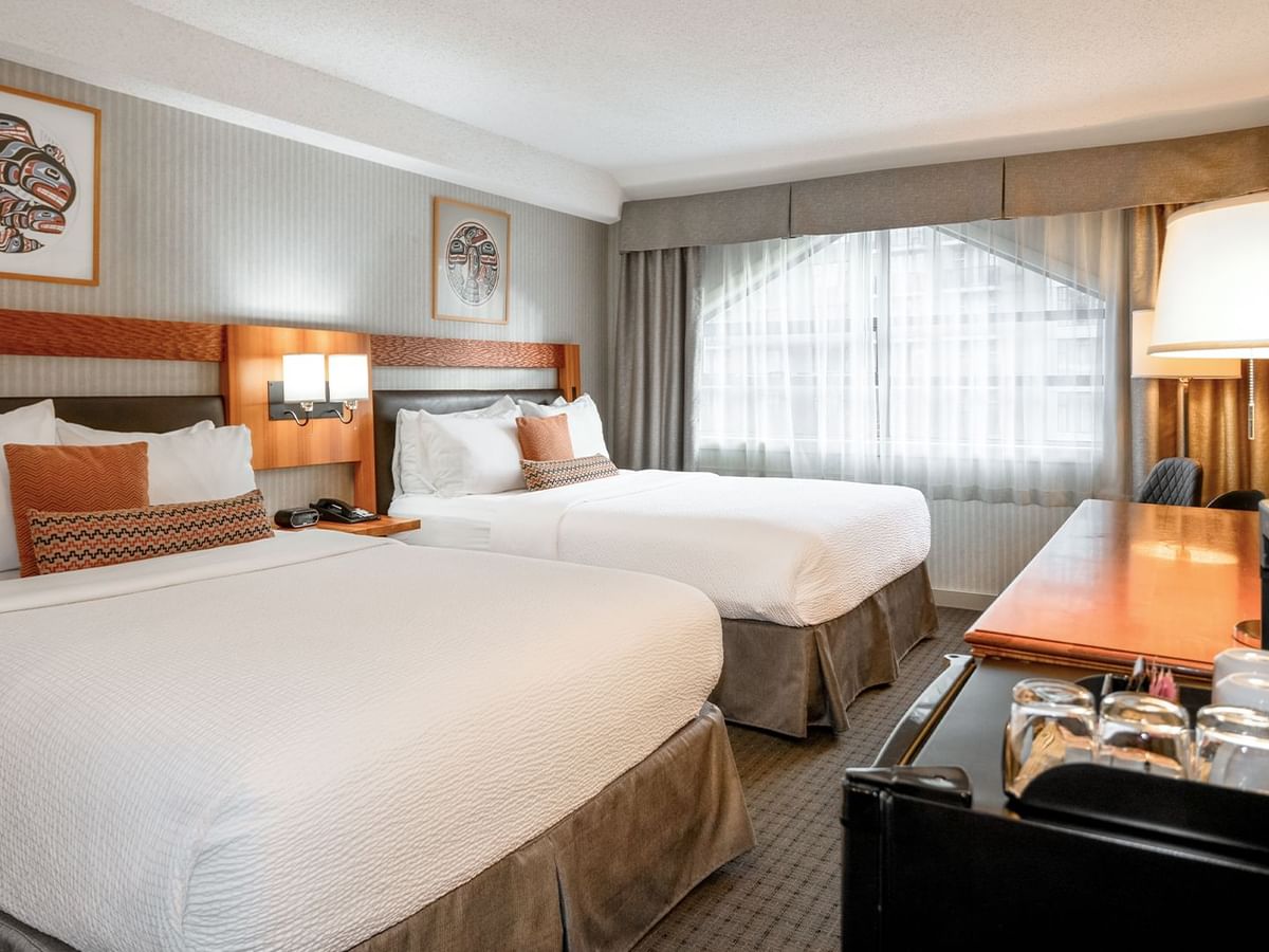 Spacious hotel room with two queen beds, HDTV, and a mini-fridge.