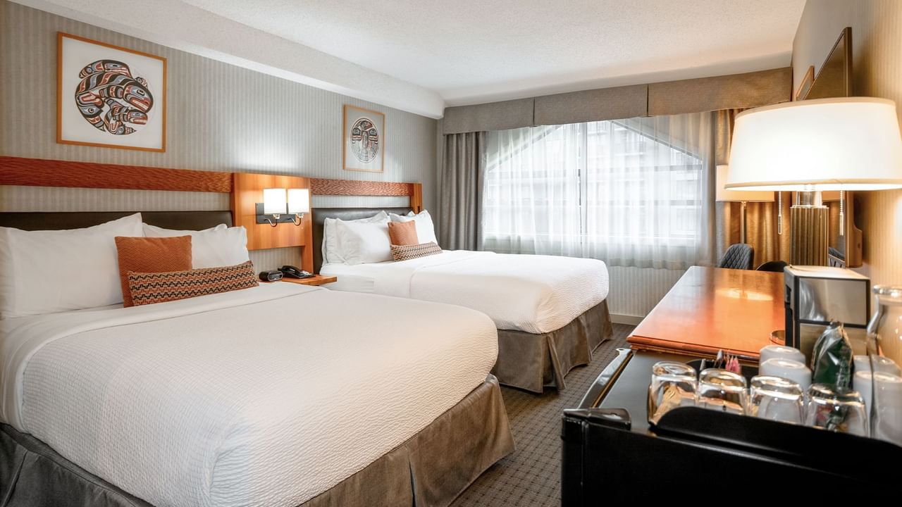 Spacious hotel room with two queen beds, HDTV, and a mini-fridge.