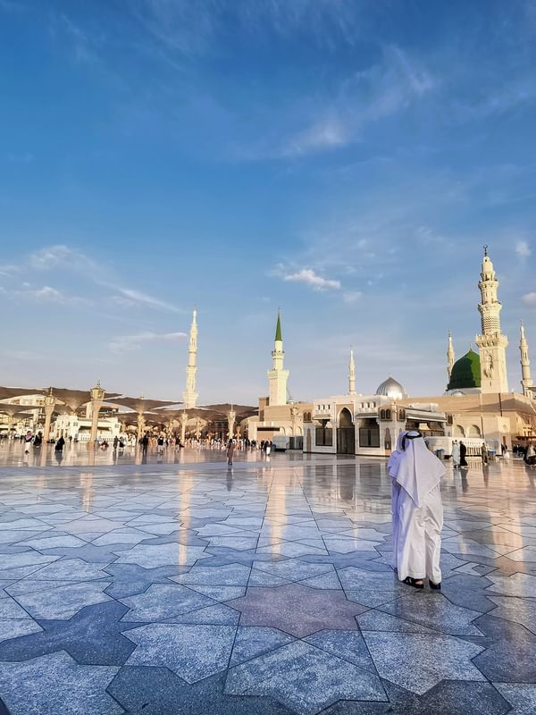 Person in traditional white robe stands in courtyard of a mosque for Eid al-Fitr celebration near Saja Warwick Madinah