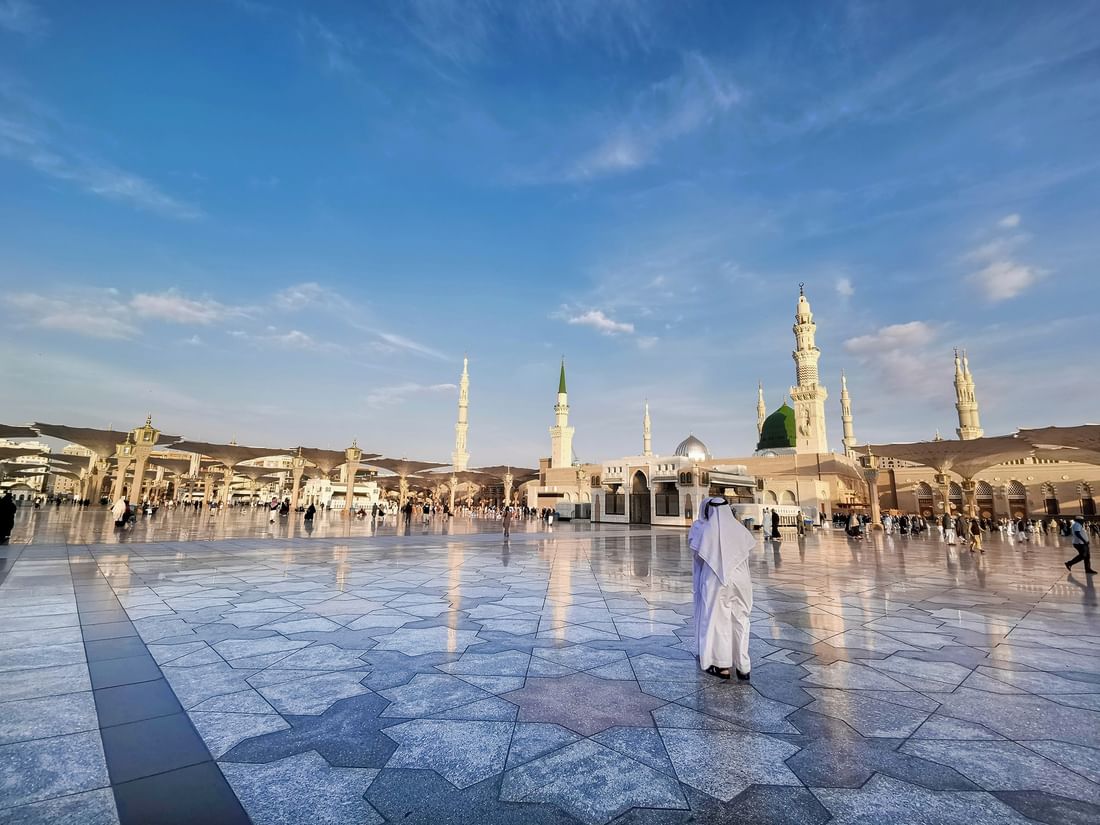 Person in traditional white robe stands in courtyard of a mosque for Eid al-Fitr celebration near Saja Warwick Madinah