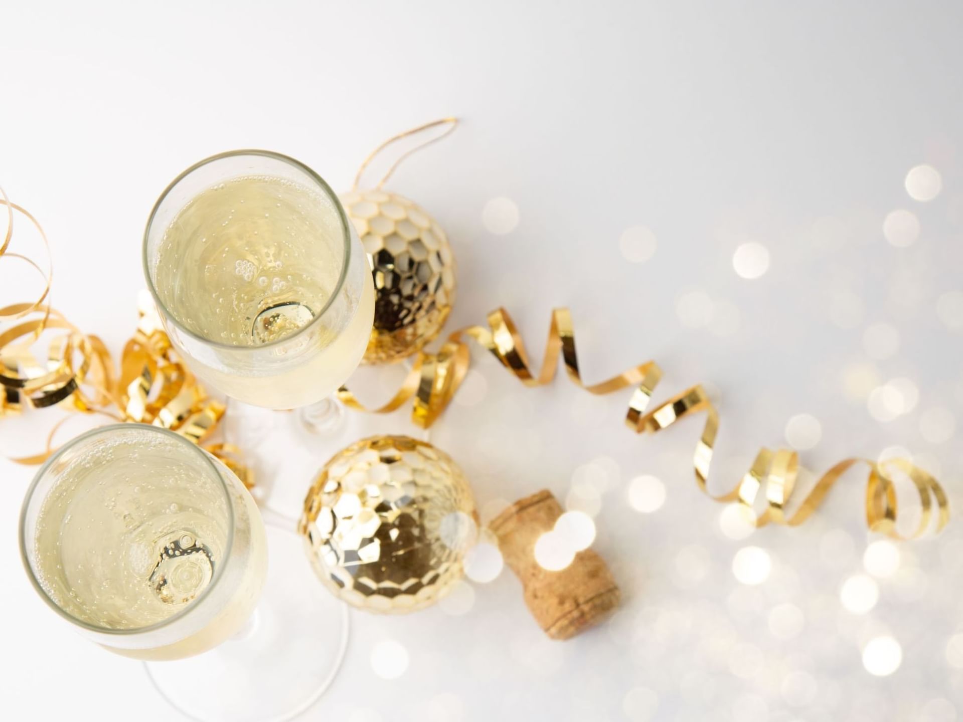 Two champagne glasses, cork, gold baubles, and ribbons on a white background at The View Hotel Eastbourne