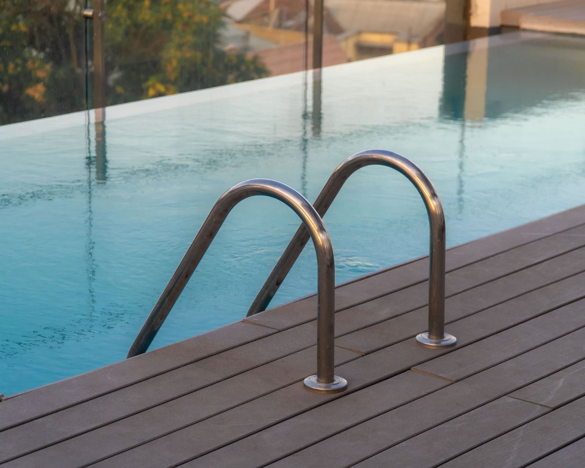 Metal pool ladder rails emerging from wooden deck beside infinity pool with glass barrier at Cumbres Lastarria