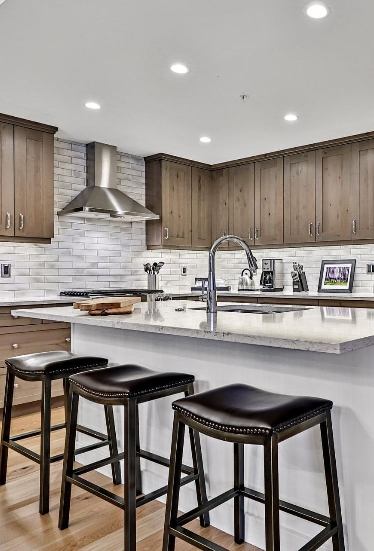 Modern kitchen with wooden cabinets, white tiles and black stools at Spring Creek Vacation Homes Canmore