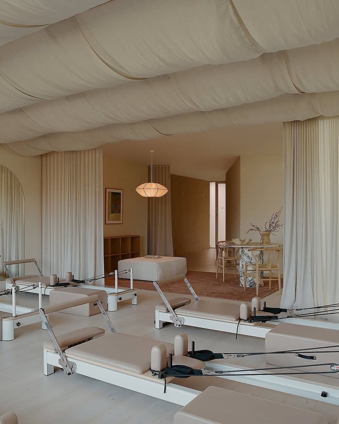 Rows of reformer beds in a calm, linen-draped pilates studio