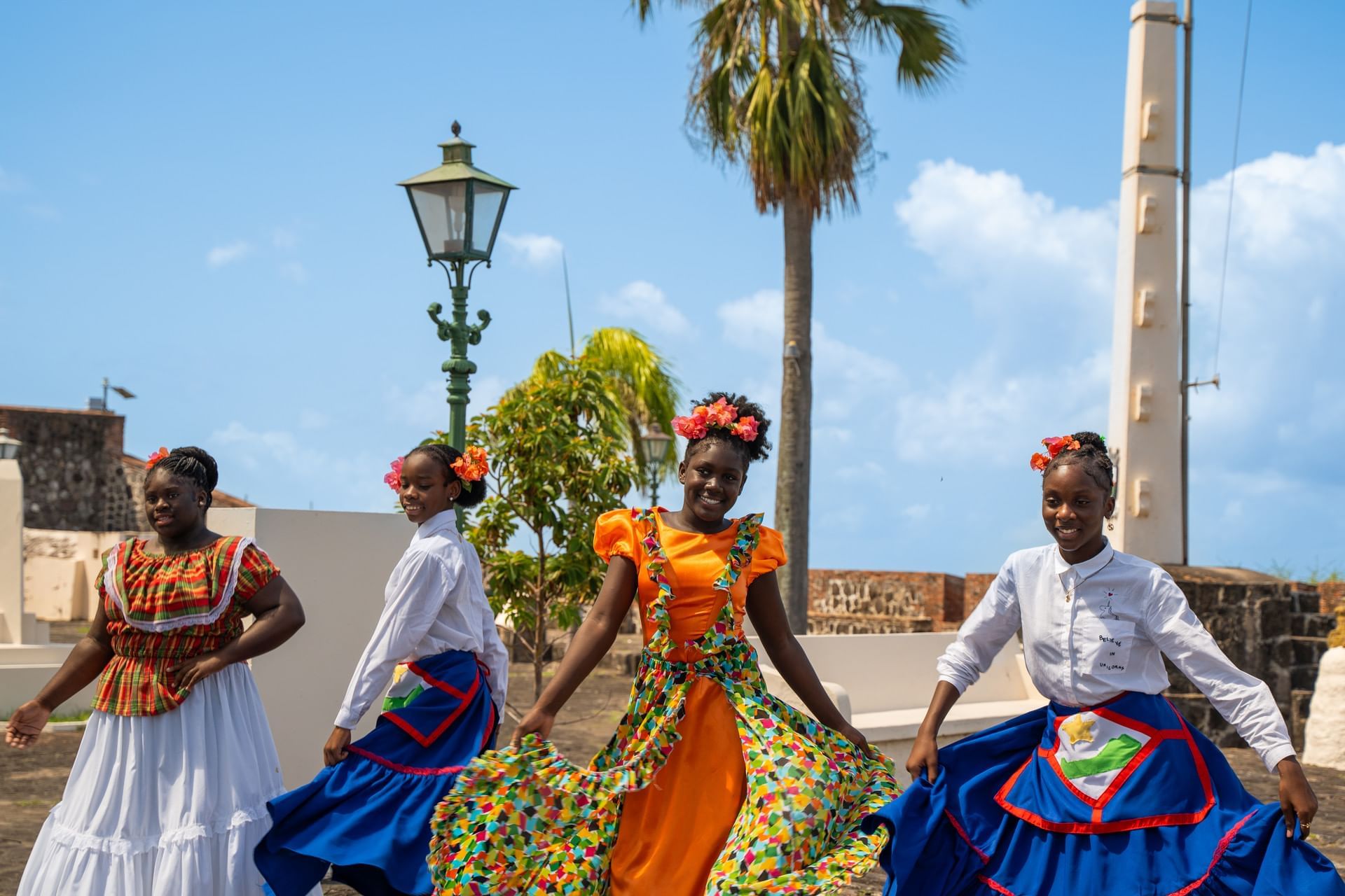 Dancers in colorful cultural dresses performing at Fort Oranje plaza near palm tree and obelisk near Golden Rock Resort