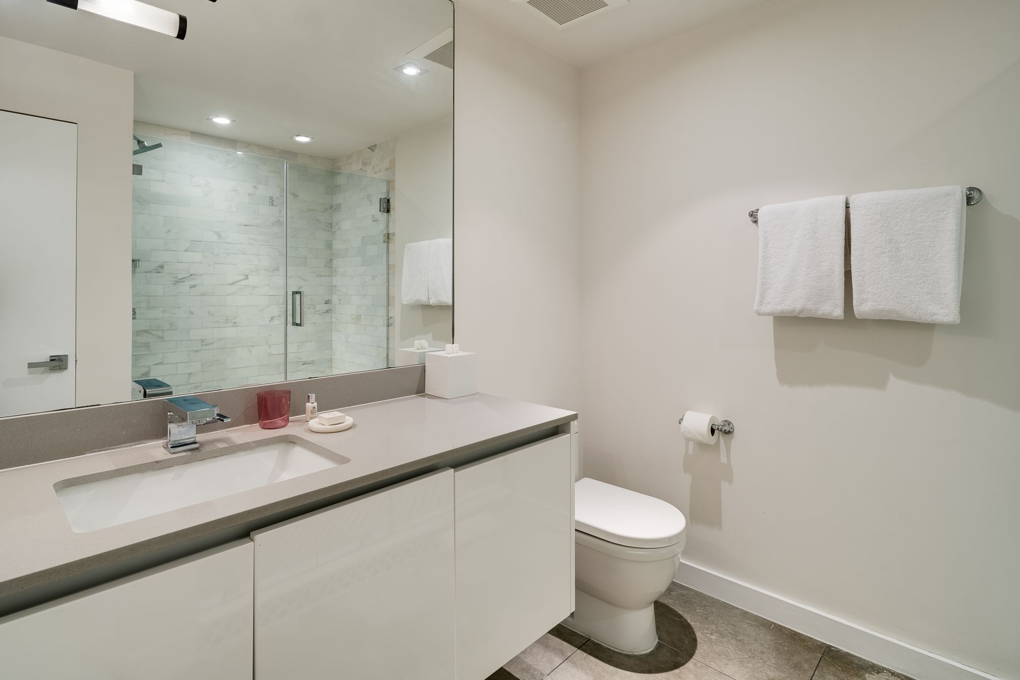 A clean and modern bathroom with a sink, toilet, shower, and towels.