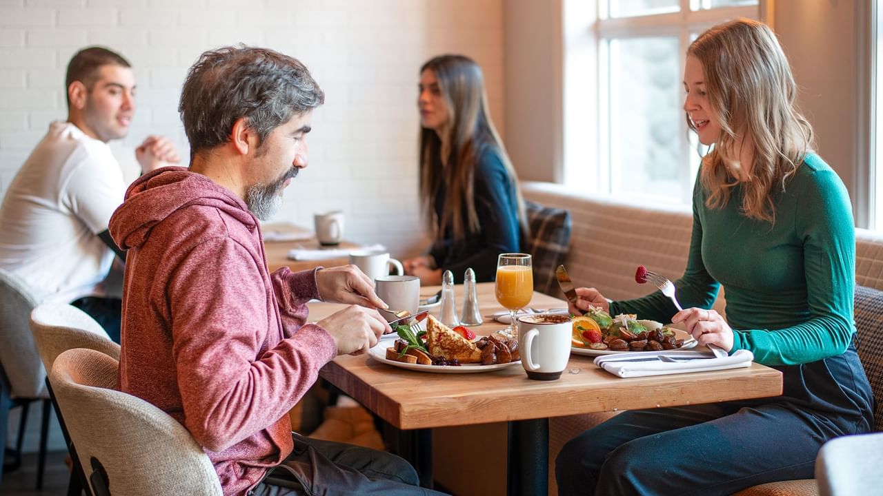 Four people eating at a restaurant table with plates of food and drinks.