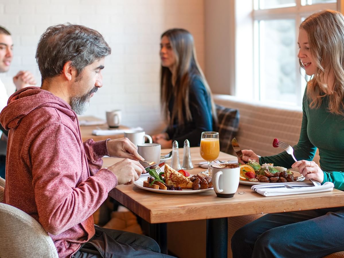 Four people are seated at a table in a dining area, eating and chatting.