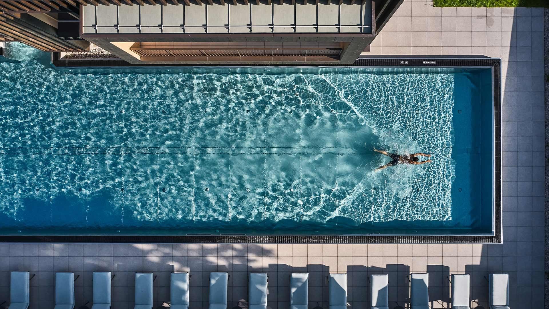 Swimmer in outdoor pool with lounge chairs at Falkensteiner Hotel Kronplatz
