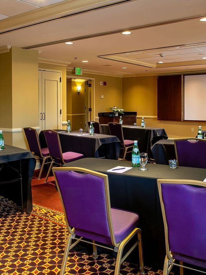 Purple chairs by black tables under a projector screen near a wooden lectern in Tabor I at Warwick Denver