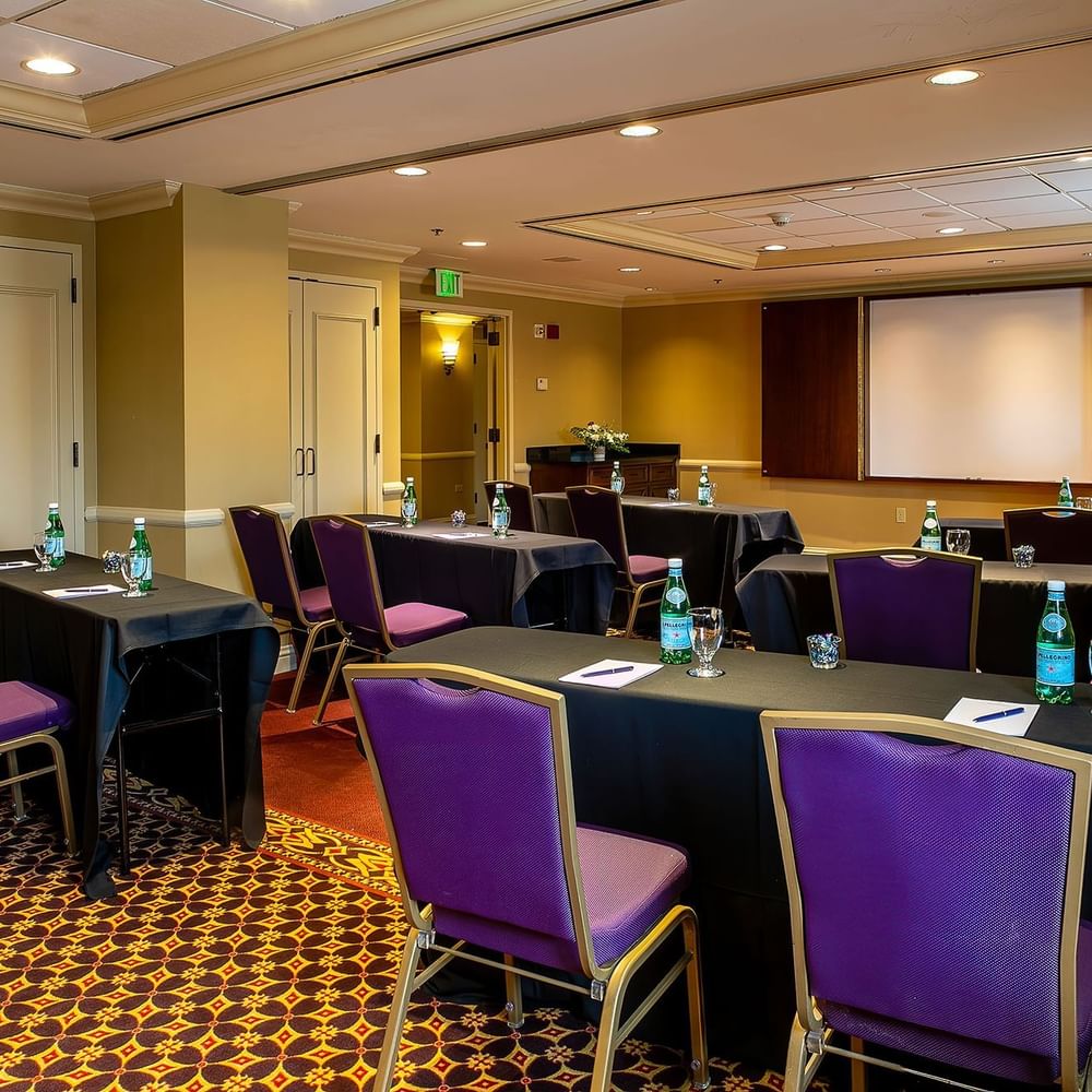 Purple chairs by black tables under a projector screen near a wooden lectern in Tabor I at Warwick Denver