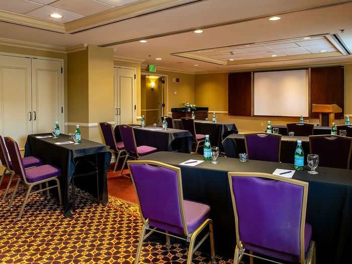 Purple chairs by black tables under a projector screen near a wooden lectern in Tabor I at Warwick Denver