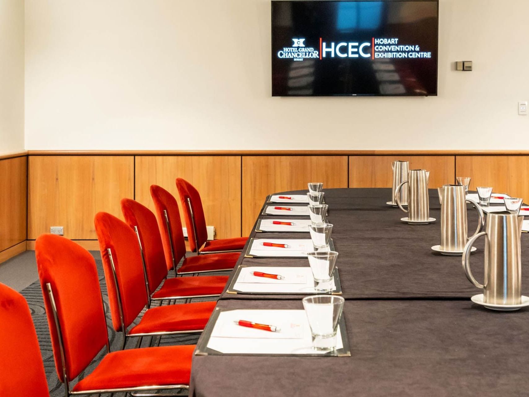 Conference set-up with red chairs and a flat screen TV in Chancellor 5 at Hotel Grand Chancellor Hobart