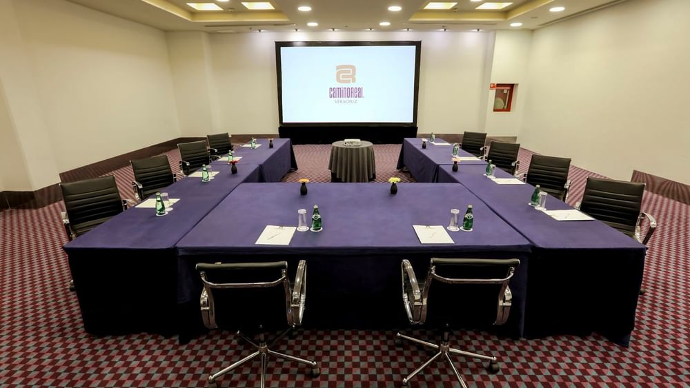 U-shape Salón del Sol meeting setup with blue linens, black chairs, and a large screen at Camino Real Veracruz