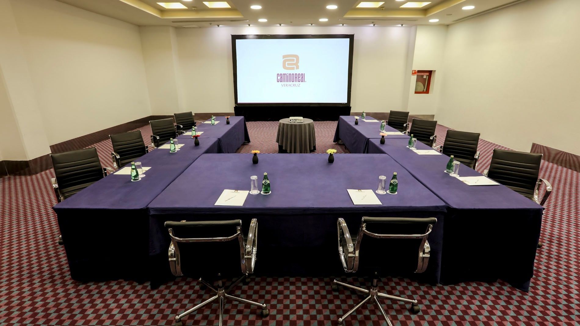 U-shape Salón del Sol meeting setup with blue linens, black chairs, and a large screen at Camino Real Veracruz