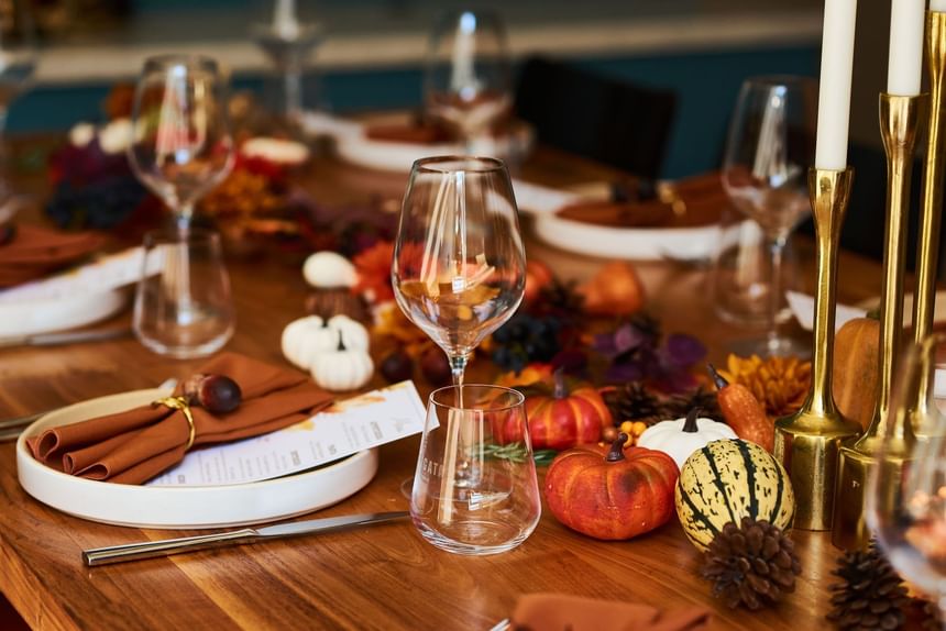 Elegant wooden table set for a meal with wine glasses, napkins, and autumn decor at the Hotel Arista.