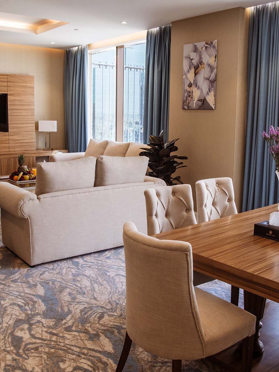 Wooden dining table by a living area with a sofa in Royal Suite at Cantonal Hotel by Warwick Riyadh