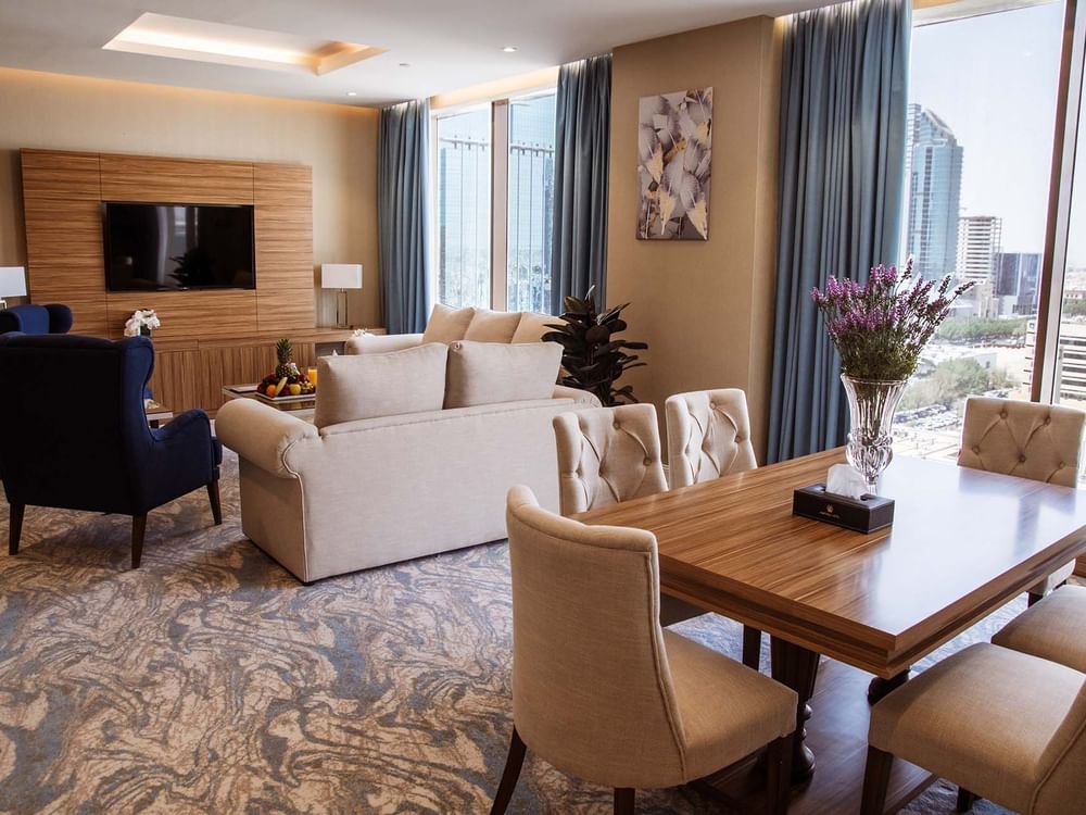 Wooden dining table by a living area with a sofa in Royal Suite at Cantonal Hotel by Warwick Riyadh