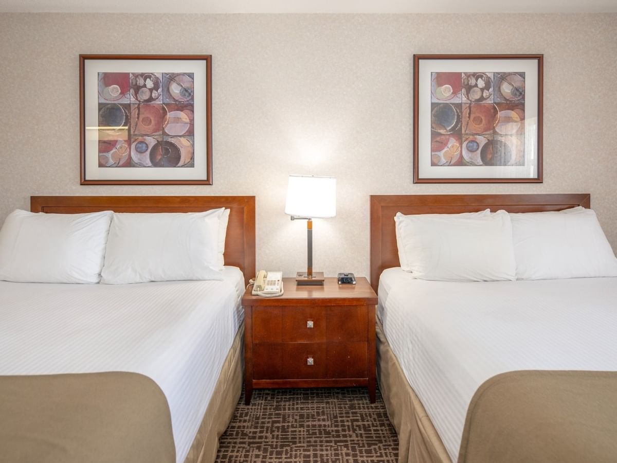 Two queen beds, a nightstand with a lamp, and framed art on the wall.
