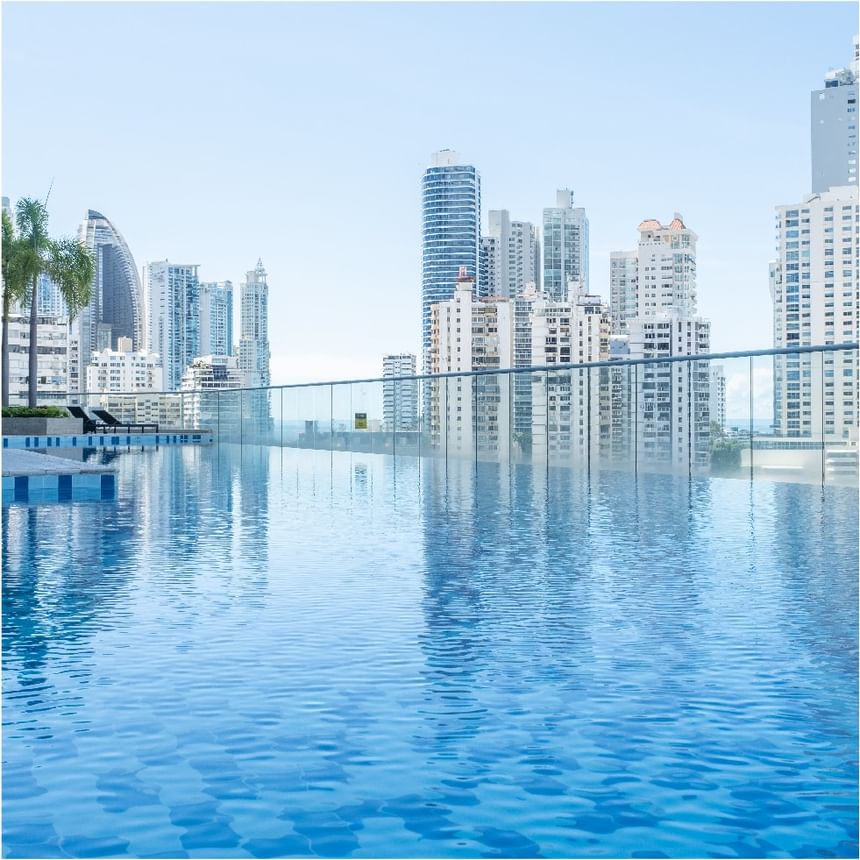 Piscina infinita de azotea con agua azul y barandillas de vidrio frente a rascacielos en Megapolis Hotel Panama
