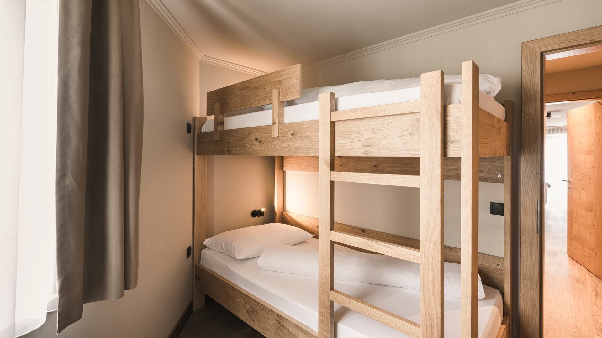 Camera familiare con letti a castello in legno e cuscini bianchi al Falkensteiner Hotel Falkensteinerhof a Valles.